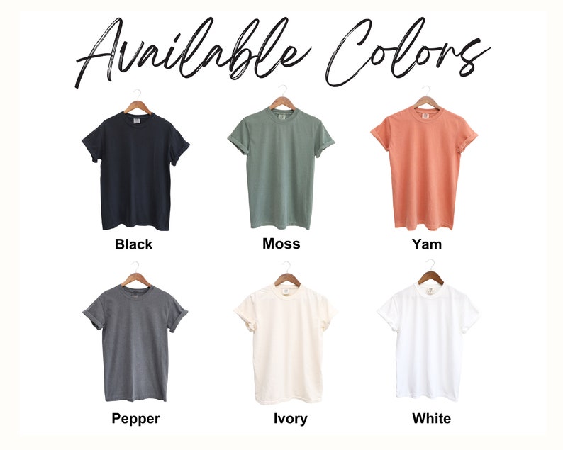 Puede incluir: Seis camisetas colgadas en perchas, mostrando diferentes colores: negro, verde musgo, coral, gris antracita, marfil y blanco. El texto "Available Colors" est&aacute; escrito encima de las camisetas.