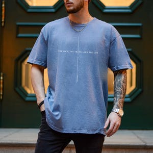 May include: A man wearing a blue t-shirt with the text "The way, the truth, and the life" printed on the front. He is wearing a silver watch on his left wrist.