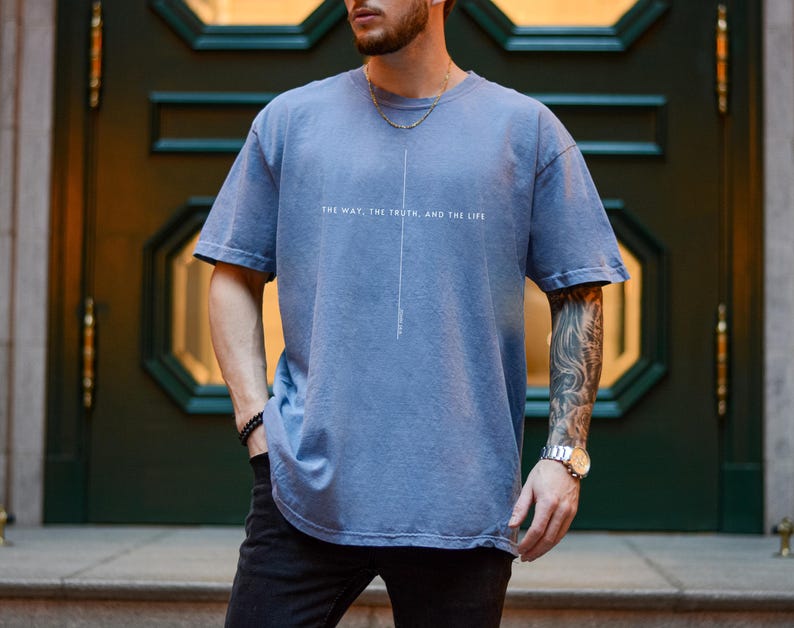 May include: A man wearing a blue t-shirt with the text "The way, the truth, and the life" printed on the front. He is wearing a silver watch on his left wrist.