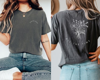 May include: A dark gray t-shirt with the text "God is good" on the front and a floral design with the text "All the time" on the back.