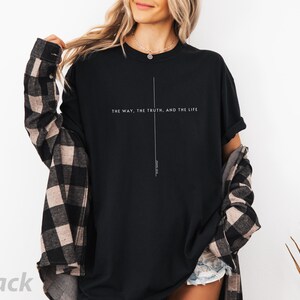 May include: Black t-shirt with the text "The way, the truth, and the life" printed on the front. The shirt is being worn by a person with a plaid shirt tied around their waist.