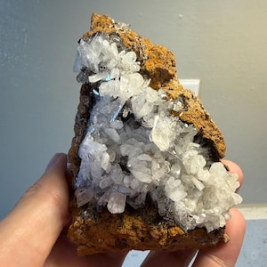 May include: A natural mineral specimen featuring clusters of clear, crystalline formations on a rough, brown matrix. The crystals are clustered together, creating a sparkling effect. The overall appearance is earthy and organic.