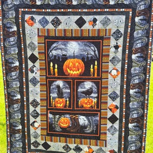 May include: A Halloween quilt in black, grey, and orange. The central panel shows a carved pumpkin, candles, and a graveyard. Other panels feature a black cat, a raven, and witch's boots. The border has repeating boot and diamond patterns. The quilt is approximately 180cm x 200cm.