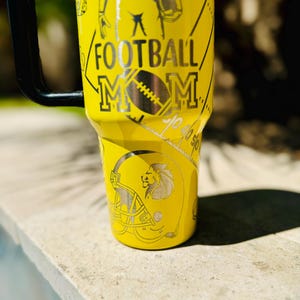 May include: Yellow stainless steel tumbler with a football player, a football helmet, and the text "FOOTBALL MOM".