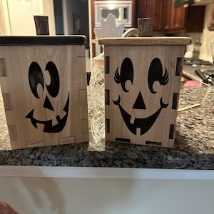 Puede incluir: Dos cajas de madera de calabaza de Halloween con caras pintadas de negro. Una caja tiene una cara sonriente con pesta&ntilde;as y la otra tiene una cara de calabaza de Halloween m&aacute;s tradicional.
