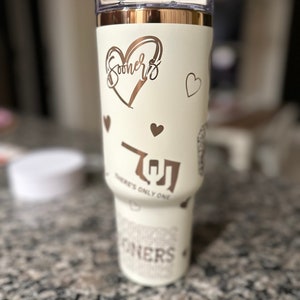 May include: White insulated tumbler with a rose gold lid and rose gold lettering. The tumbler features a heart with the word "Sooners" inside, a heart with the letter "O" inside, and the text "There's Only One".