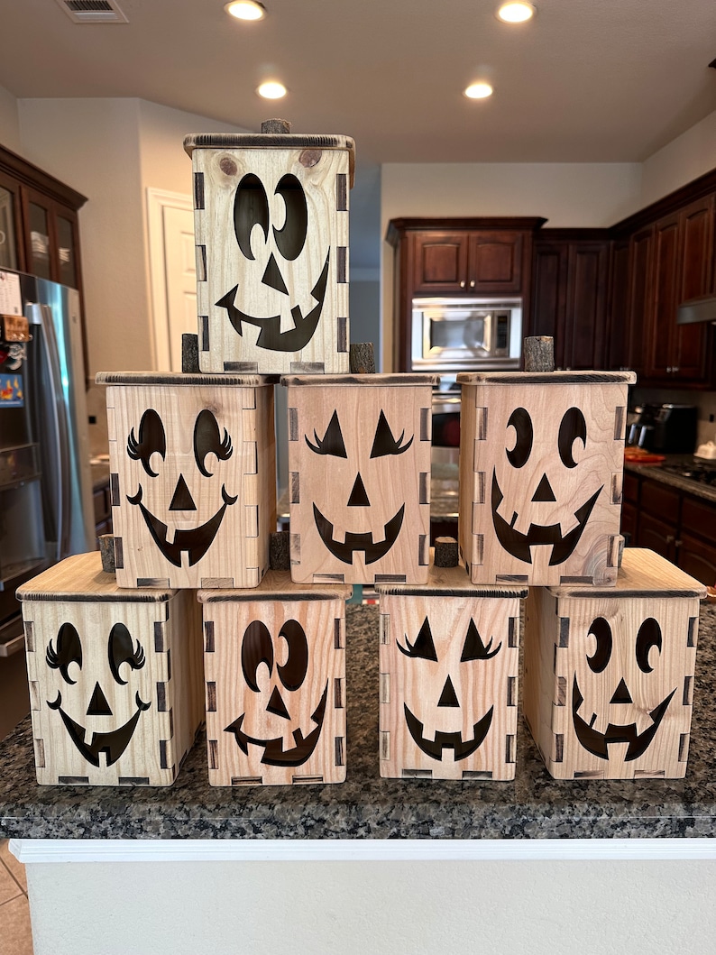 Puede incluir: Ocho cajas de madera de calabaza de Halloween con diferentes expresiones faciales. Las cajas est&aacute;n apiladas en forma de pir&aacute;mide y son de madera marr&oacute;n claro.