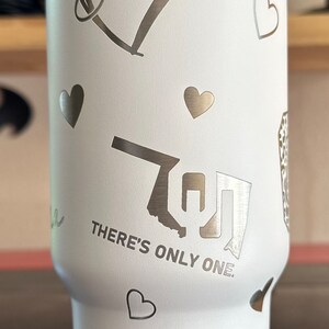 May include: White stainless steel travel mug with a heart design and the words "Sooners" and "There's Only One." The mug also features a repeated pattern of the word "Sooners" around the bottom.