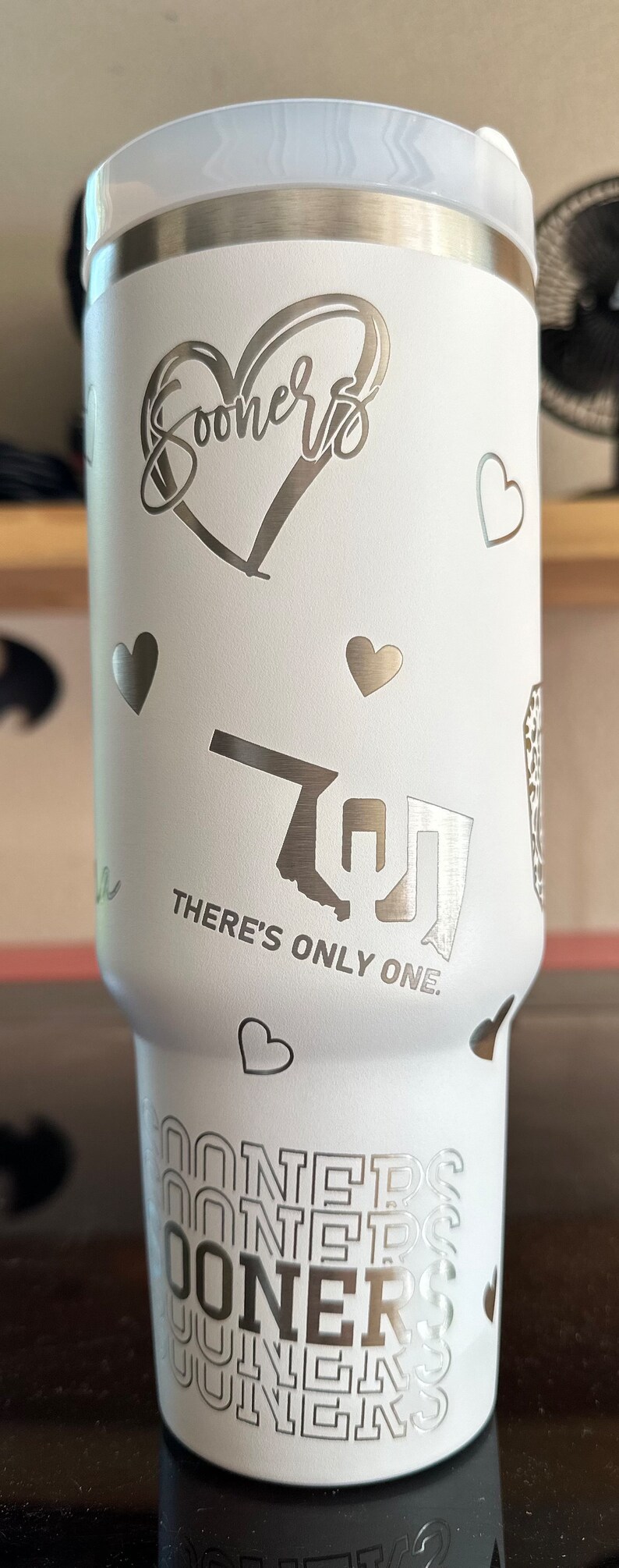 May include: White stainless steel travel mug with a heart design and the words "Sooners" and "There's Only One." The mug also features a repeated pattern of the word "Sooners" around the bottom.