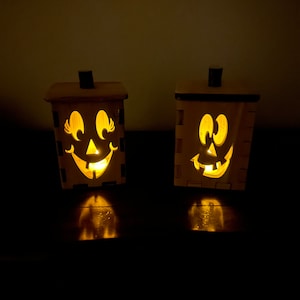 Puede incluir: Dos portavelas de madera con forma de calabaza con caras talladas y velas encendidas en su interior.