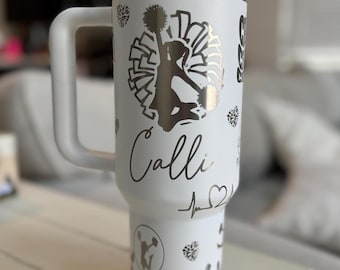 May include: White stainless steel tumbler with a black and white cheerleader design. The tumbler has a handle and a lid. The name "Calli" is written on the tumbler.