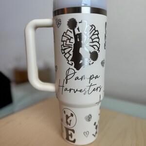 May include: White stainless steel travel mug with a black and white cheerleader graphic, the text "Pampa Harvesters", and a black and white pom-pom design.