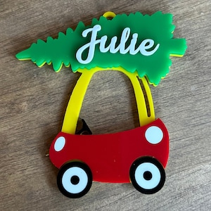 May include: A red toy car with yellow wheels and a green Christmas tree on top. The tree has the name "Julie" written on it in white.