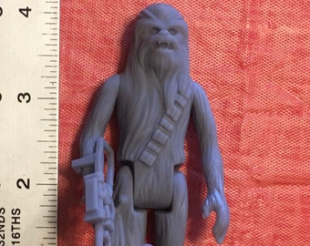 May include: A gray plastic action figure of Chewbacca from Star Wars. He is holding a blaster rifle and has a bandolier across his chest.