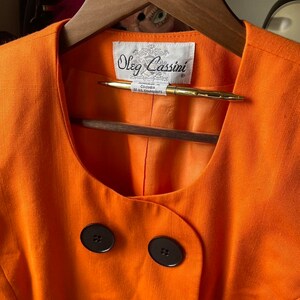 May include: Orange linen blazer with a scoop neck and two black buttons. The label reads "Oleg Cassini" with the words "Registered in Colombia" and "Design U.S. Patents" underneath.