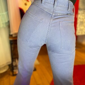 May include: Light blue denim jeans with a high waist and a classic five-pocket design. The jeans have a straight leg and a Wrangler label on the back pocket. The fabric appears to be a medium-weight denim.