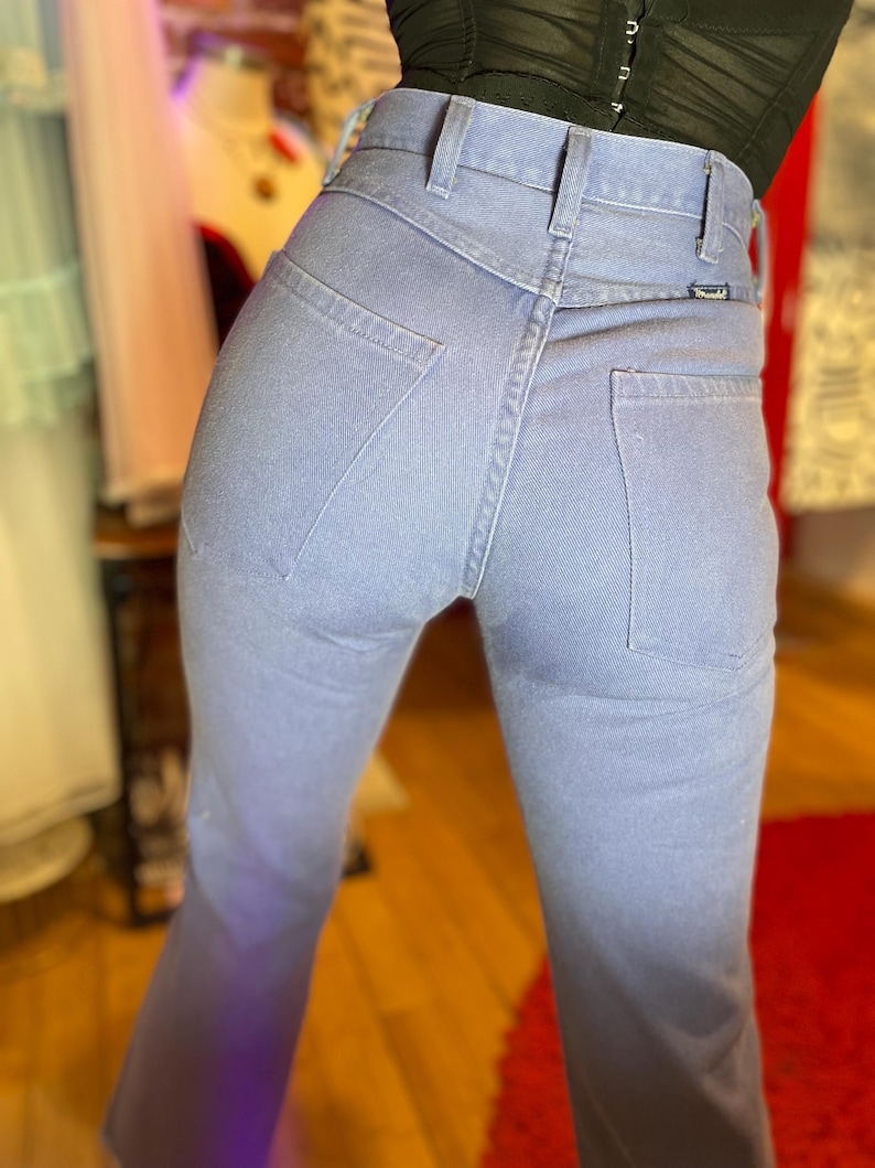 May include: Light blue denim jeans with a high waist and a classic five-pocket design. The jeans have a straight leg and a Wrangler label on the back pocket. The fabric appears to be a medium-weight denim.