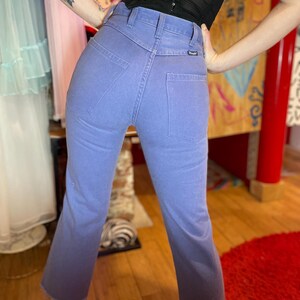 May include: Light blue denim jeans with a high waist and a slight flare at the hem. The jeans have a Wrangler label and classic five-pocket styling. The denim has a faded, ombre effect, transitioning to a darker shade at the bottom.