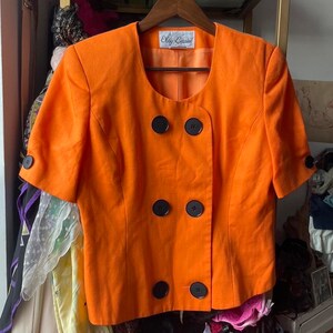 May include: Orange short-sleeved blazer with black buttons and a label that reads "Oleg Cassini".