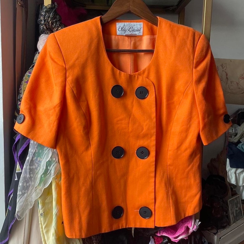 May include: Orange short-sleeved blazer with black buttons and a label that reads "Oleg Cassini".