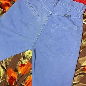 May include: Light blue denim jeans with a classic five-pocket design. The jeans feature a straight leg cut and a Wrangler brand label on the back pocket. The fabric appears to be a sturdy cotton blend.