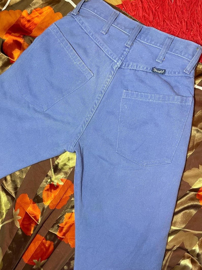 May include: Light blue denim jeans with a classic five-pocket design. The jeans feature a straight leg cut and a Wrangler brand label on the back pocket. The fabric appears to be a sturdy cotton blend.