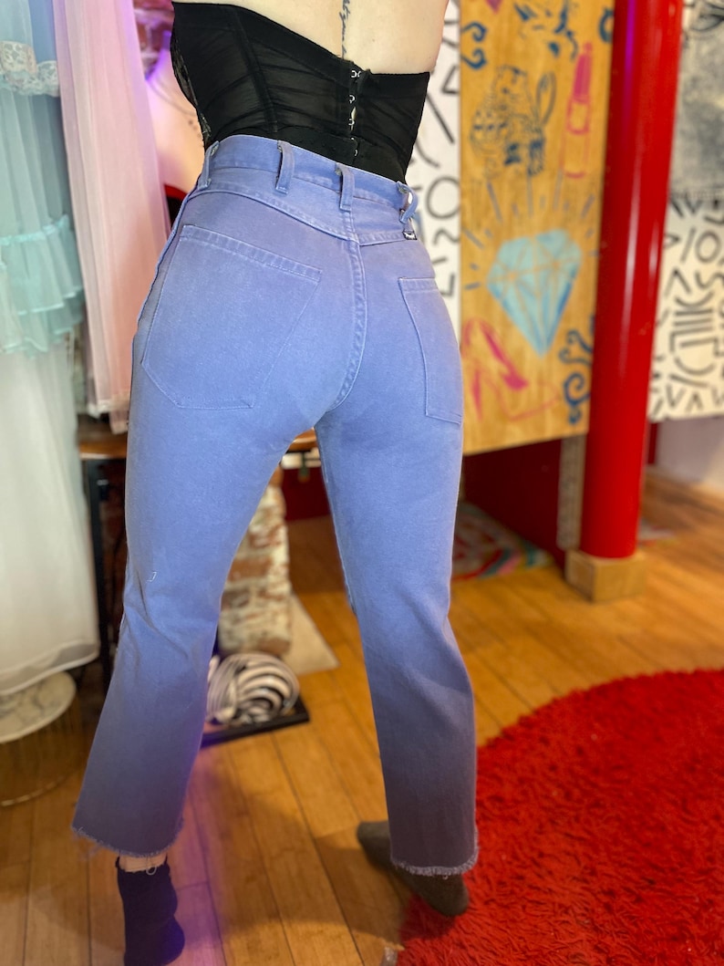 May include: Light blue denim jeans with a high waist and a slight flare at the ankle. The jeans have a faded, ombre effect, transitioning from light blue to a darker shade at the hem. The jeans have classic five-pocket styling.