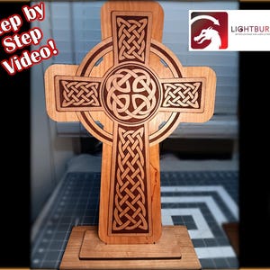 May include: A wooden Celtic cross with intricate knotwork designs, standing on a wooden base. The cross is light brown with darker etched details. Text in the image reads "Step by Step Video!" and a logo for Lightburn is visible.