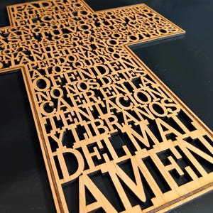 May include: A wooden cross with cut-out text in a script font. The cross is made of light-colored wood and the text is in Spanish. The text includes the words "Padre Nuestro" and "Amen".