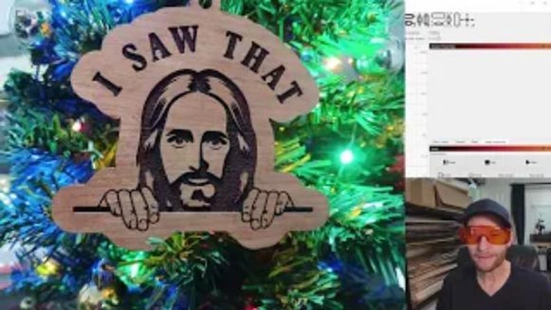 May include: Wooden Christmas ornament with the phrase "I SAW THAT" and an image of Jesus. The ornament is hanging on a Christmas tree with blue and green lights. The ornament is made of light brown wood.
