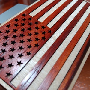 May include: A wooden American flag with red and white stripes and a field of blue stars. The stars are cut out of the wood, creating a unique and decorative design.