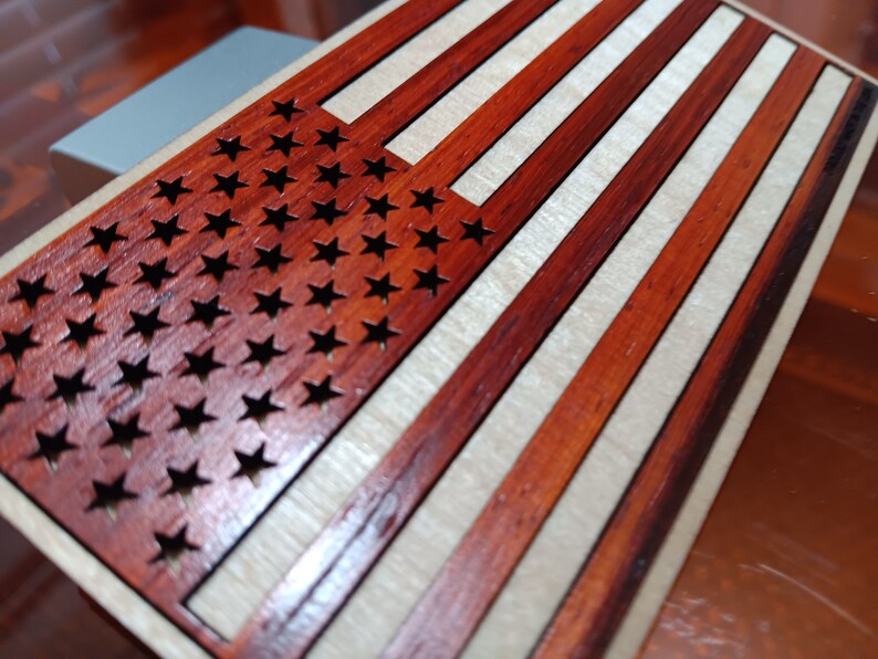 May include: A wooden American flag with red and white stripes and a field of blue stars. The stars are cut out of the wood, creating a unique and decorative design.