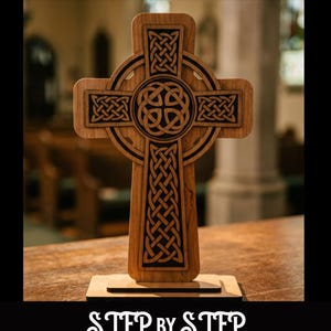 May include: A wooden Celtic cross with intricate knotwork designs. The cross is displayed on a wooden base. The image includes the text "SVG & Lightburn" and "Step by Step Video For LASERS".