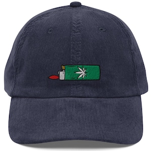May include: Navy blue corduroy baseball cap with an embroidered design of a green lighter with a cannabis leaf and red flame. The cap has a curved brim and a fabric strap closure.