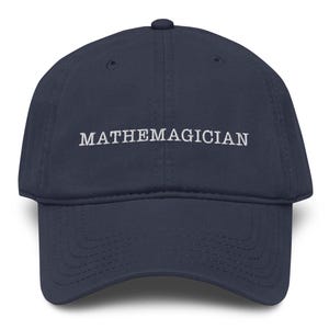 May include: Navy blue baseball cap with the word "MATHEMAGICIAN" embroidered in white. The cap has a curved brim and an adjustable strap at the back. A classic, casual accessory.