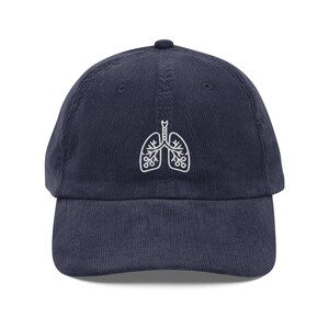 May include: Navy blue corduroy baseball cap featuring a white embroidered lung design. The cap has a curved brim and an adjustable strap at the back. A stylish and comfortable accessory.