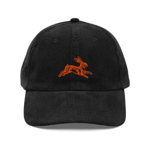 May include: Black corduroy baseball cap featuring an embroidered orange rabbit design. The cap has a curved brim and an adjustable strap at the back. A stylish accessory for casual wear.
