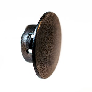 Może przedstawiać: Czarna plastikowa zaślepka z fakturowaną powierzchnią i dwoma małymi otworami. Zaślepka jest przeznaczona do zakrycia otworu lub szczeliny.