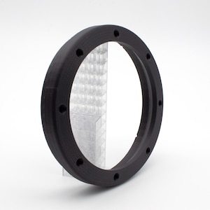 May include: Black plastic ring with a circular opening and multiple small holes around the edge. The ring is designed to fit around a speaker.
