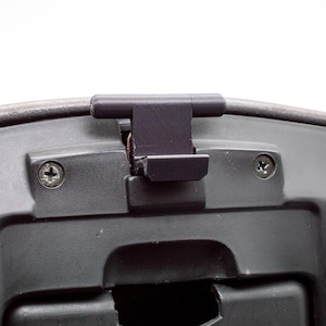 Może przedstawiać: Zbliżenie czarnego plastikowego elementu samochodu z ciemnoszarym wykończeniem. Element posiada mechanizm zatrzaskowy i jest mocowany za pomocą śrub. Tło jest jednolicie białe.