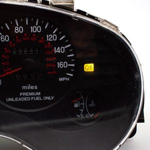 Może przedstawiać: Zbliżenie deski rozdzielczej samochodu. Prędkościomierz wskazuje 0 mph, a licznik przebiegu 24844. Deska rozdzielcza zawiera wskaźniki paliwa i temperatury, a wskaźnik świateł przeciwmgielnych jest podświetlony.