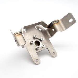 Może przedstawiać: Srebrny metalowy wspornik z okrągłym otworem i pięcioma śrubami. Wspornik ma wygięty ramion, który wystaje w prawo.