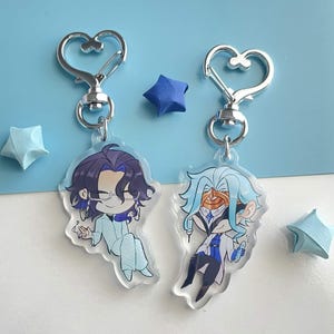 May include: Two clear acrylic keychains featuring chibi-style anime characters with heart-shaped silver metal clasps. One character has dark purple hair and glasses, while the other has light blue hair and a mask, both attached to silver rings.