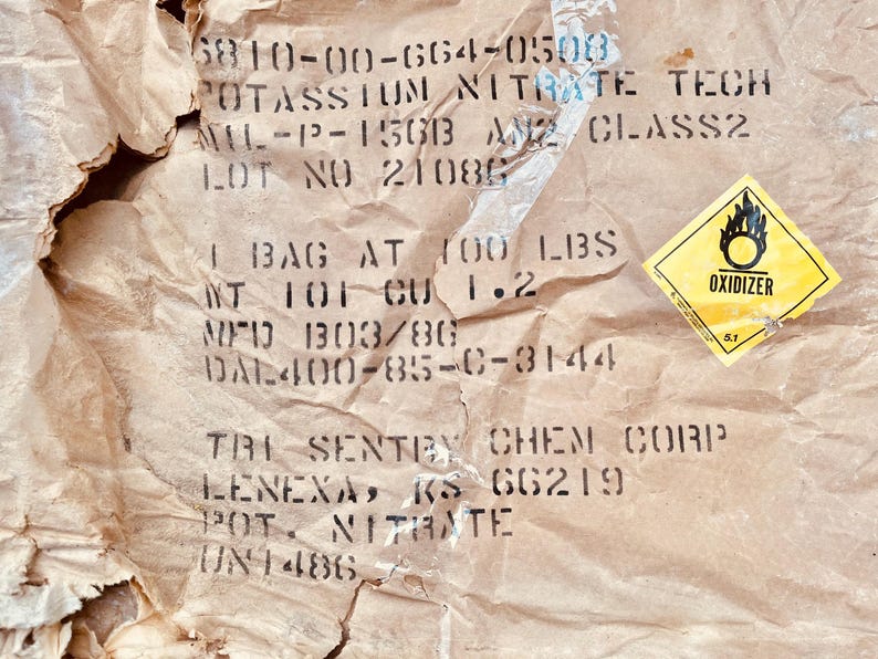 May include: A brown paper bag with the text "POTASSIUM NITRATE TECH" and "LOT NO 21080". The bag also has a yellow warning label with the text "OXIDIZER".