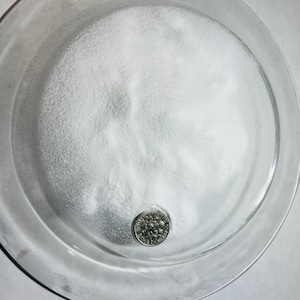 May include: A white powder in a clear glass dish with a US dime for scale.