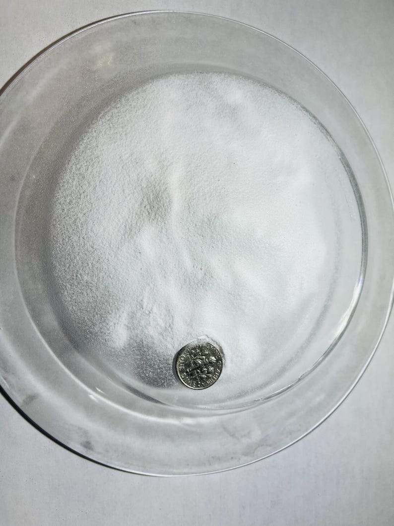 May include: A white powder in a clear glass dish with a US dime for scale.
