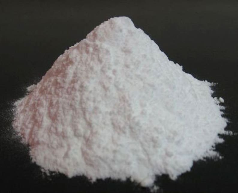 May include: A close-up of a pile of white powder on a black surface. The powder is fine and smooth, and it appears to be very dry.