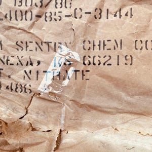 May include: Close-up of a brown paper bag with black text that reads "TRI-SENTRY CHEM CORP LENEXA, KS 66219 POT NITRATE 701-486".