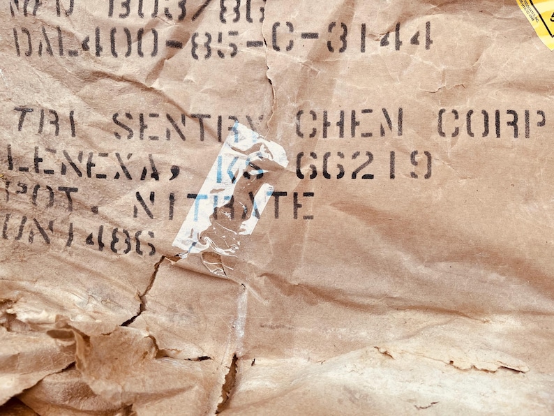 May include: Close-up of a brown paper bag with black text that reads "TRI-SENTRY CHEM CORP LENEXA, KS 66219 POT NITRATE 701-486".