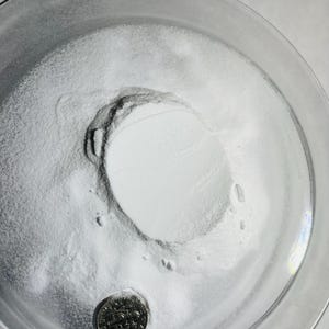 May include: A white powder in a clear glass bowl with a US quarter coin for scale.